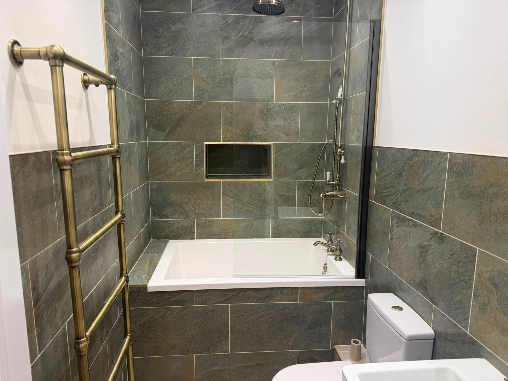 Slate-tiled bathroom with brass shower fittings and inset shelf niche