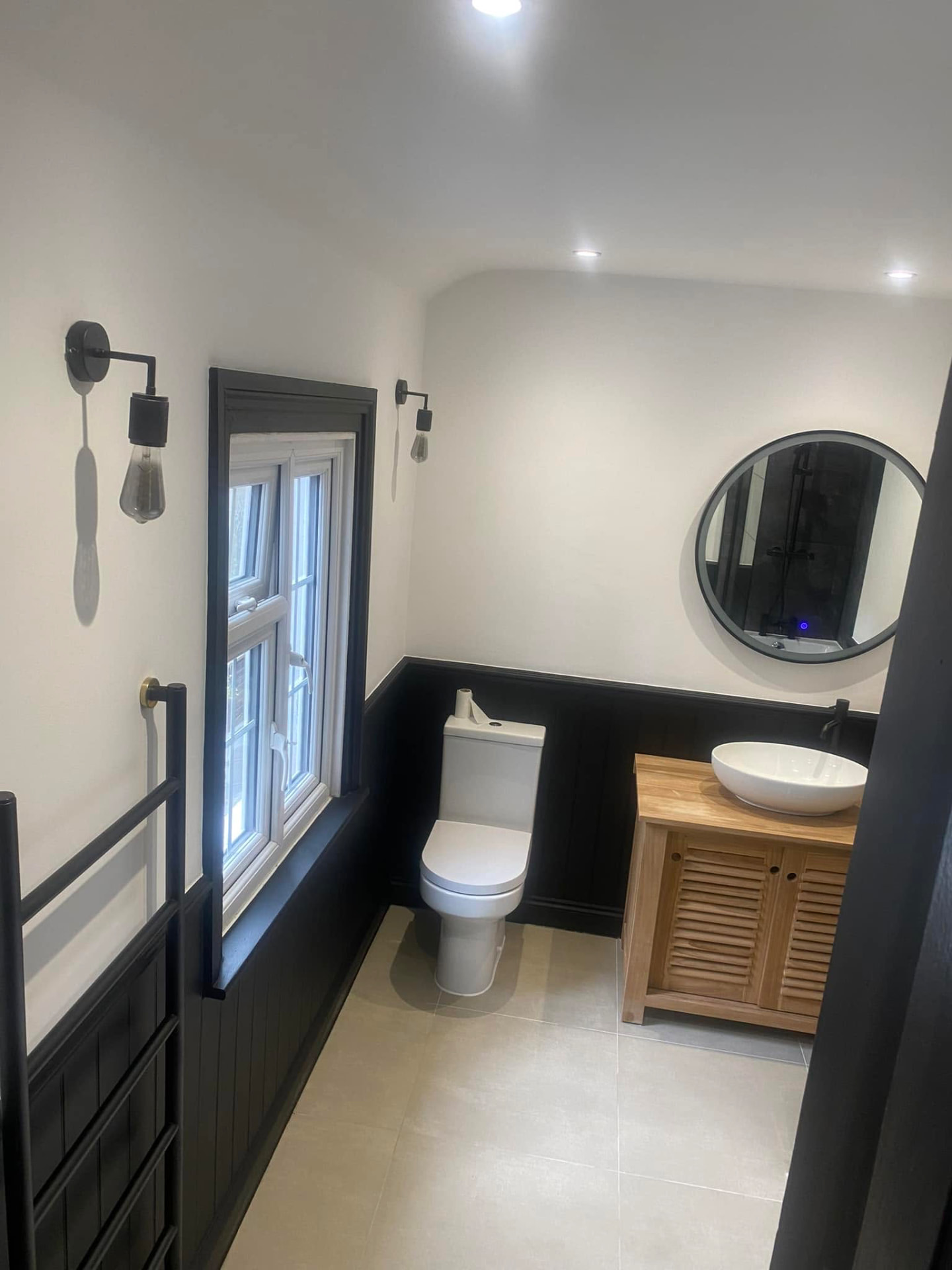 Bathroom with black panelling, oak vanity and round backlit mirror