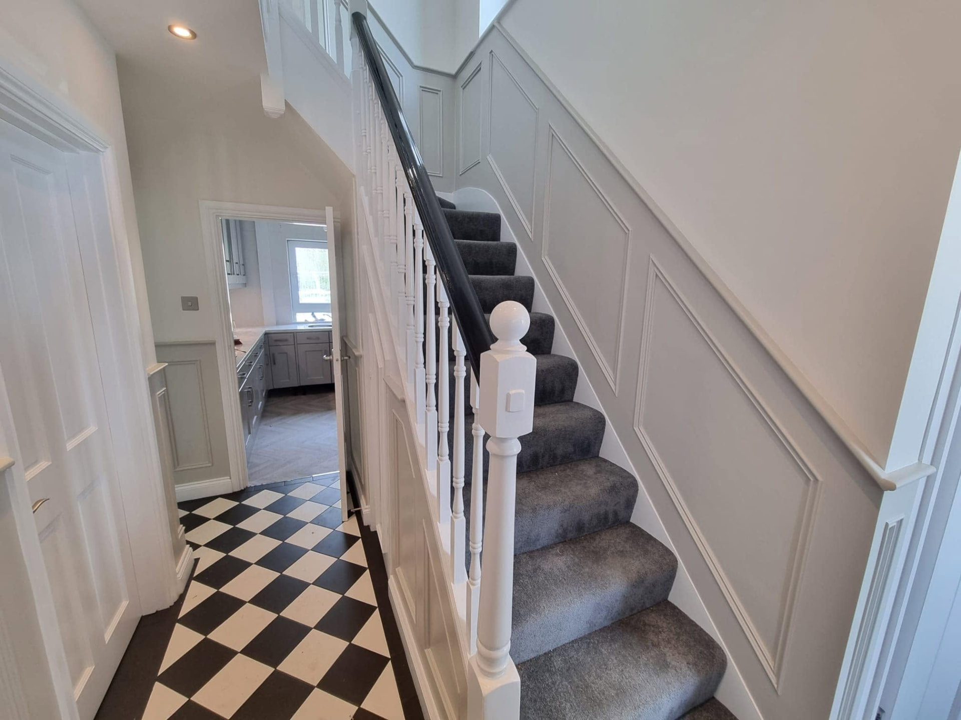 Refurbished hallway with panelled walls, chequerboard tiled floor and painted staircase