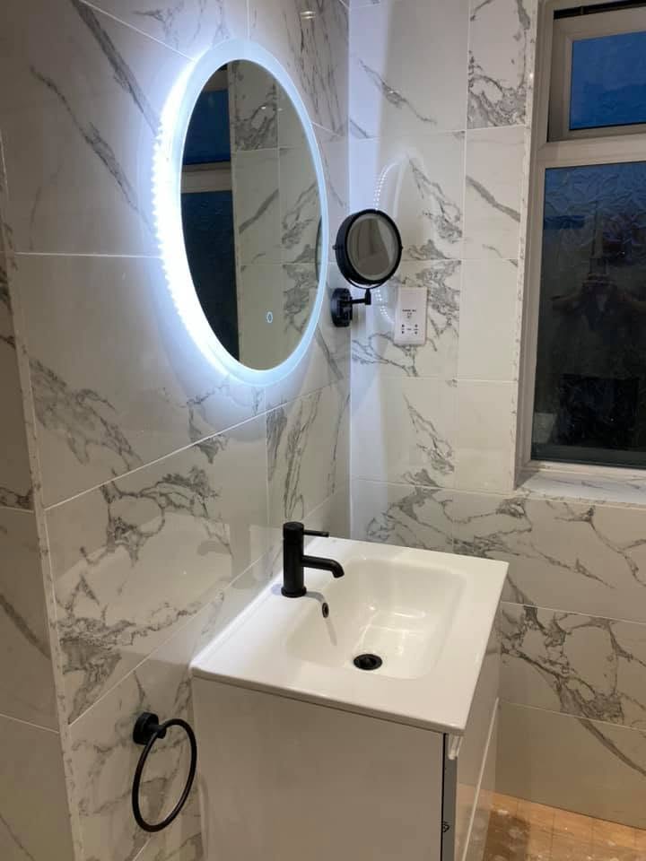 Marble-tiled cloakroom with backlit round mirror and black tapware